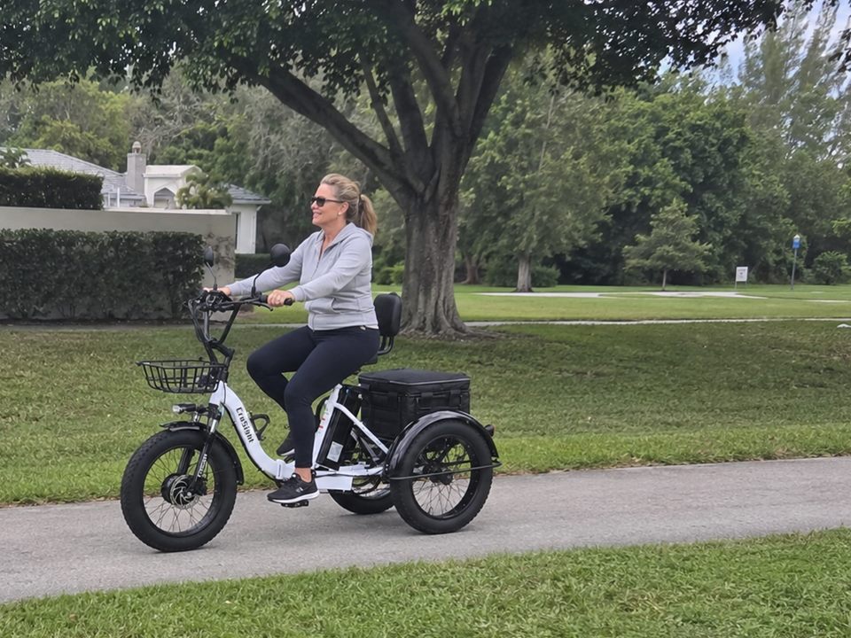 CroSight customer riding a white electric trike along a grassy community path.