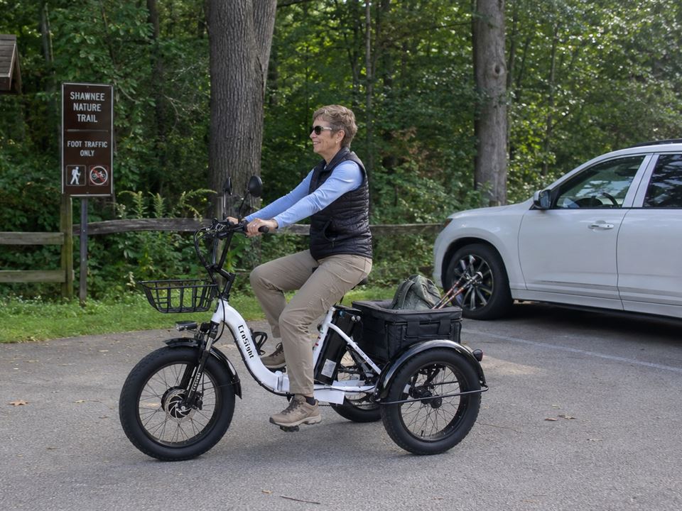CroSight customer riding a white electric trike near a nature trail entrance.
