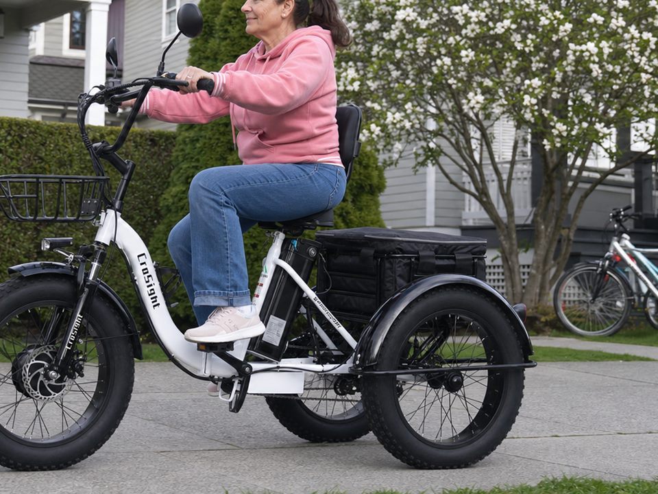 CroSight customer in a pink jacket riding a white electric trike on a community path.