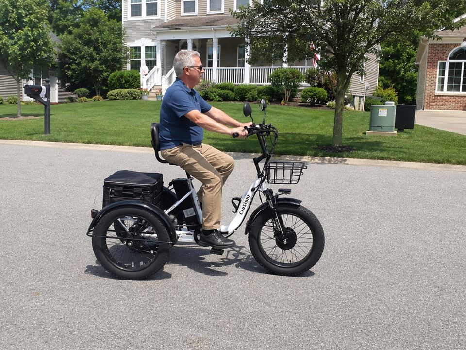 CroSight customer riding a white electric trike on a sunny residential street.