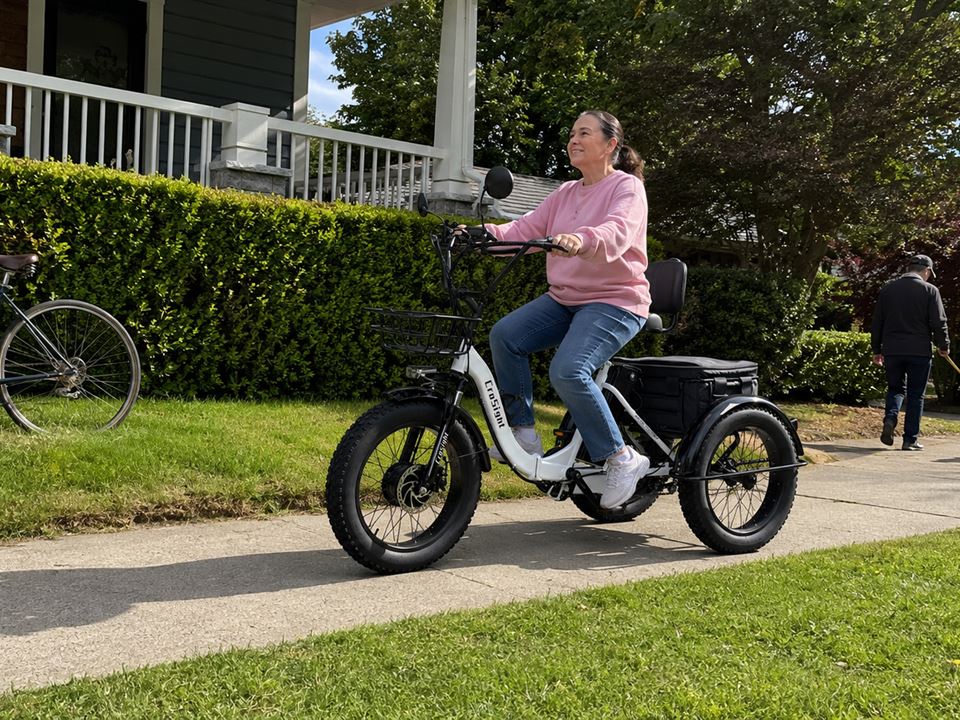 CroSight customer riding a white electric trike on a sunny neighborhood sidewalk.