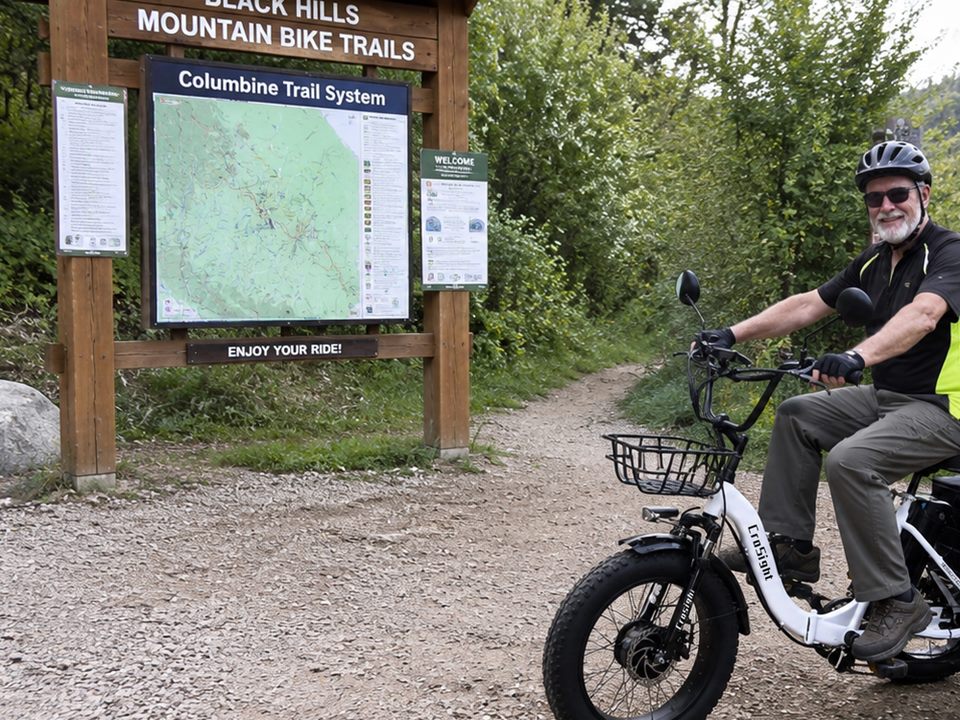 CroSight customer riding a white electric trike near a mountain trail sign.